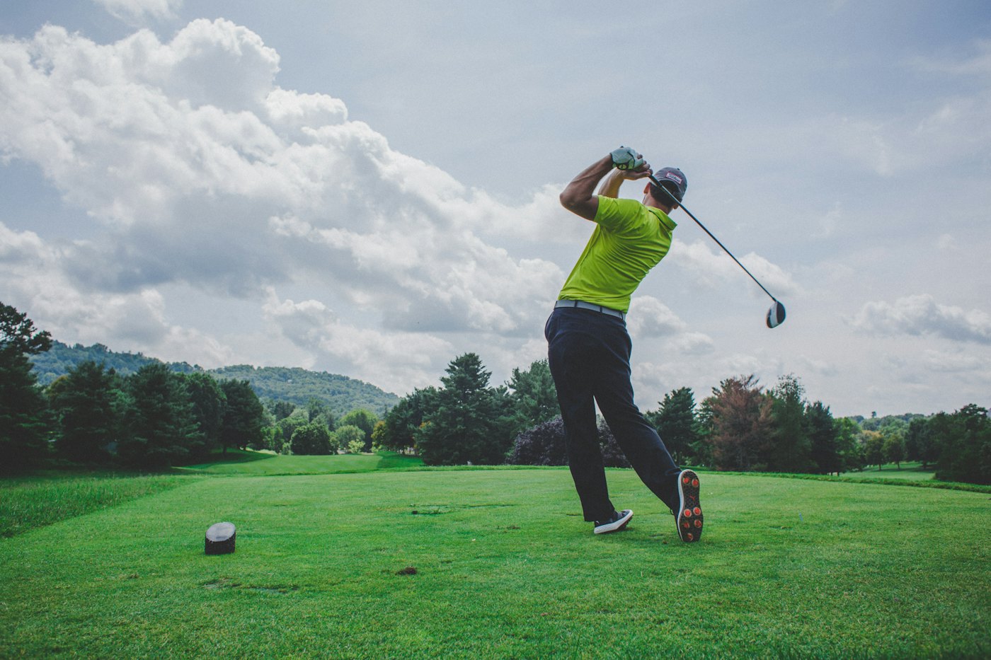 Golfeur à l'attaque d'un coup de départ sur un parcours, face aux collines