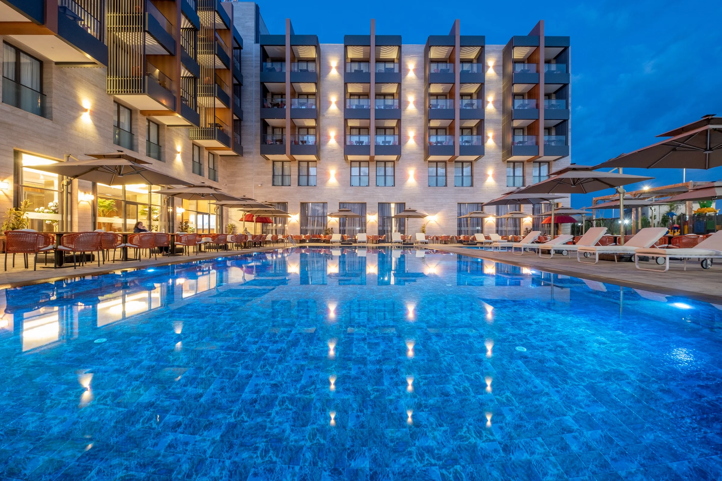 La piscine extérieure et la façade de l'hôtel illuminées à la tombée de la nuit